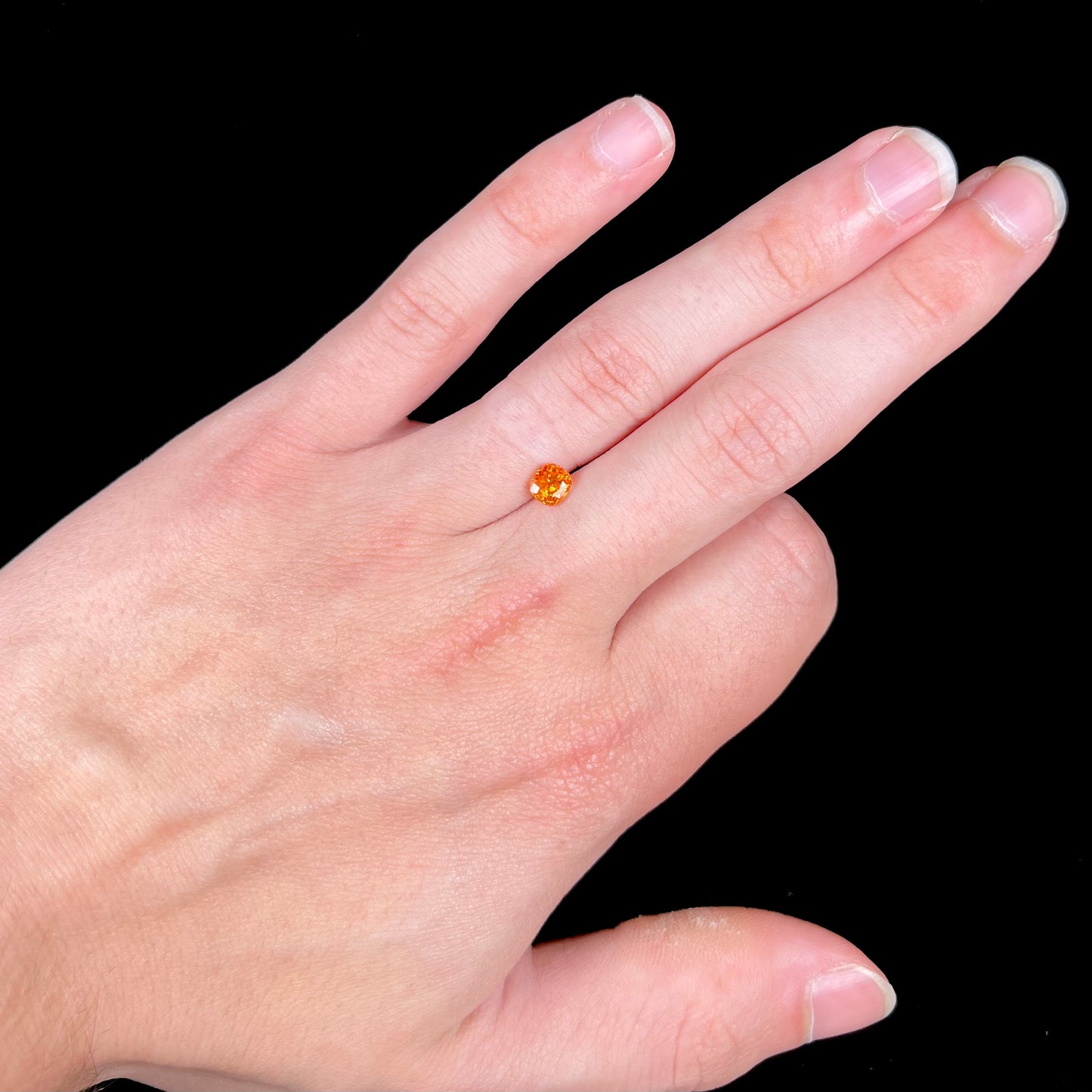 A faceted cushion cut natural orange sapphire gemstone.  The stone is cut to enhance the orange color.