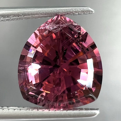 A loose, rounded trillion shield cut pink tourmaline gemstone.