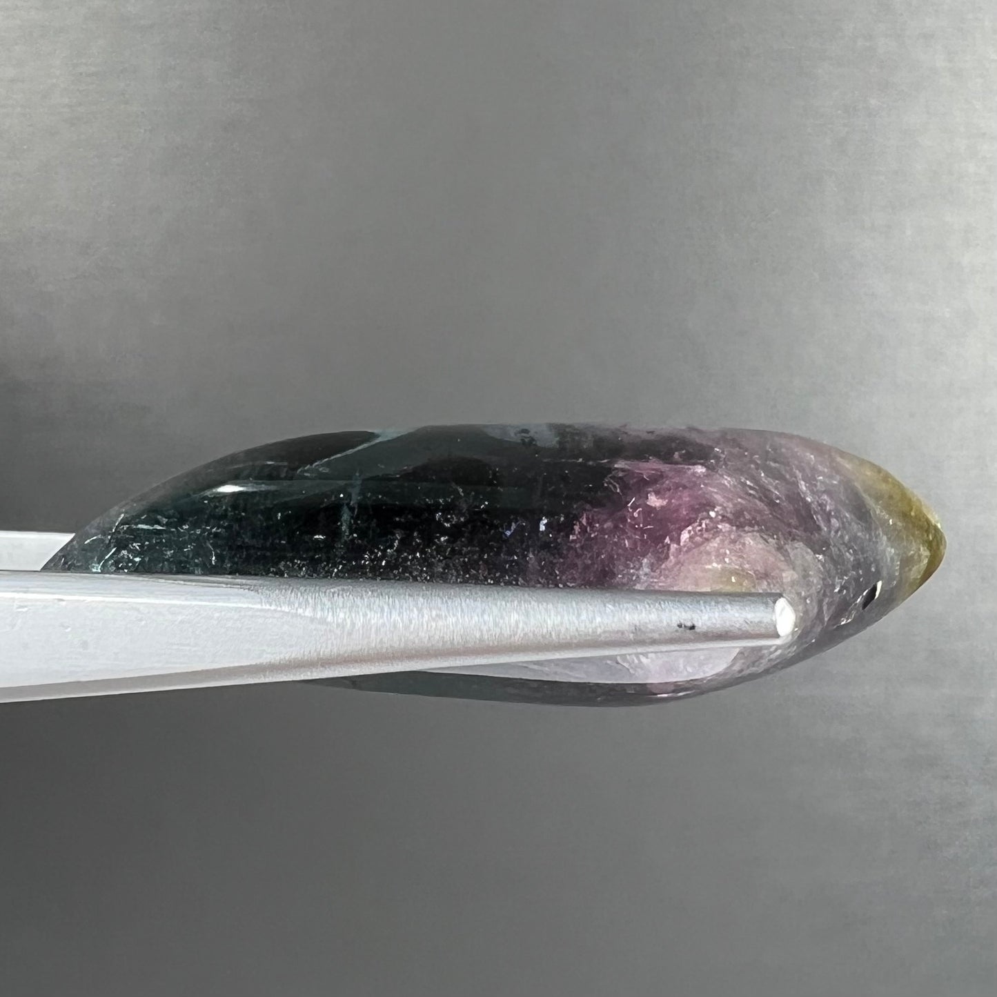 A loose, freeform cabochon cut tricolor tourmaline stone that has blue, pink, and yellow colors.
