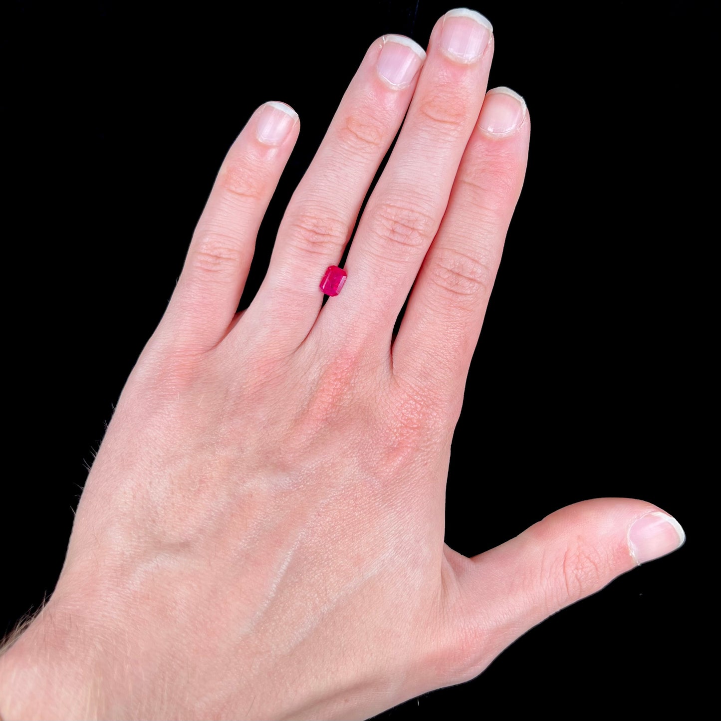 An emerald cut Burma ruby gemstone.  The stone is loose and a pinkish red color.