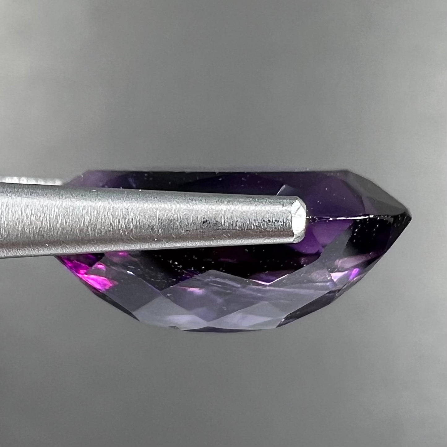 A loose, faceted oval cut Siberian amethyst gemstone.  The stone is purple color with blue and red flashes.