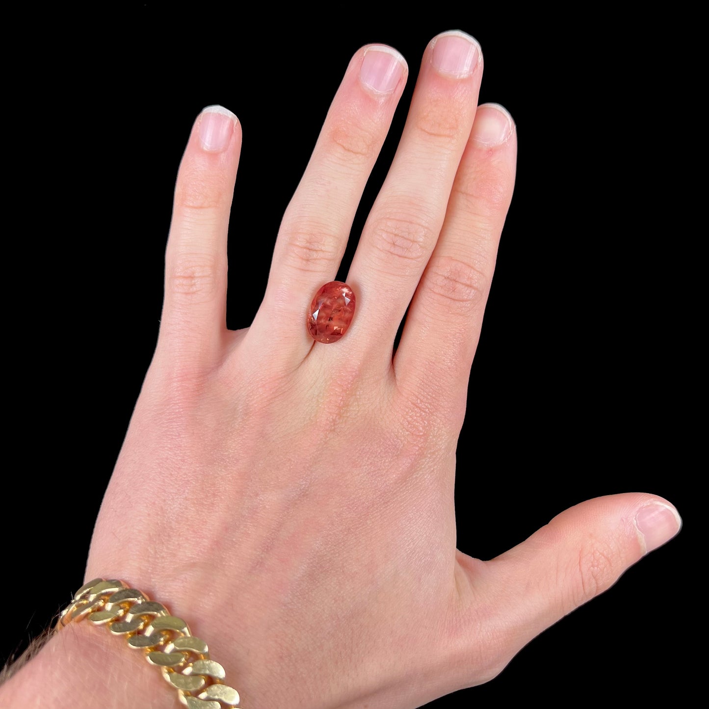 A faceted, oval cut sunstone.  The stone is red-orange color with a bright schiller flash.