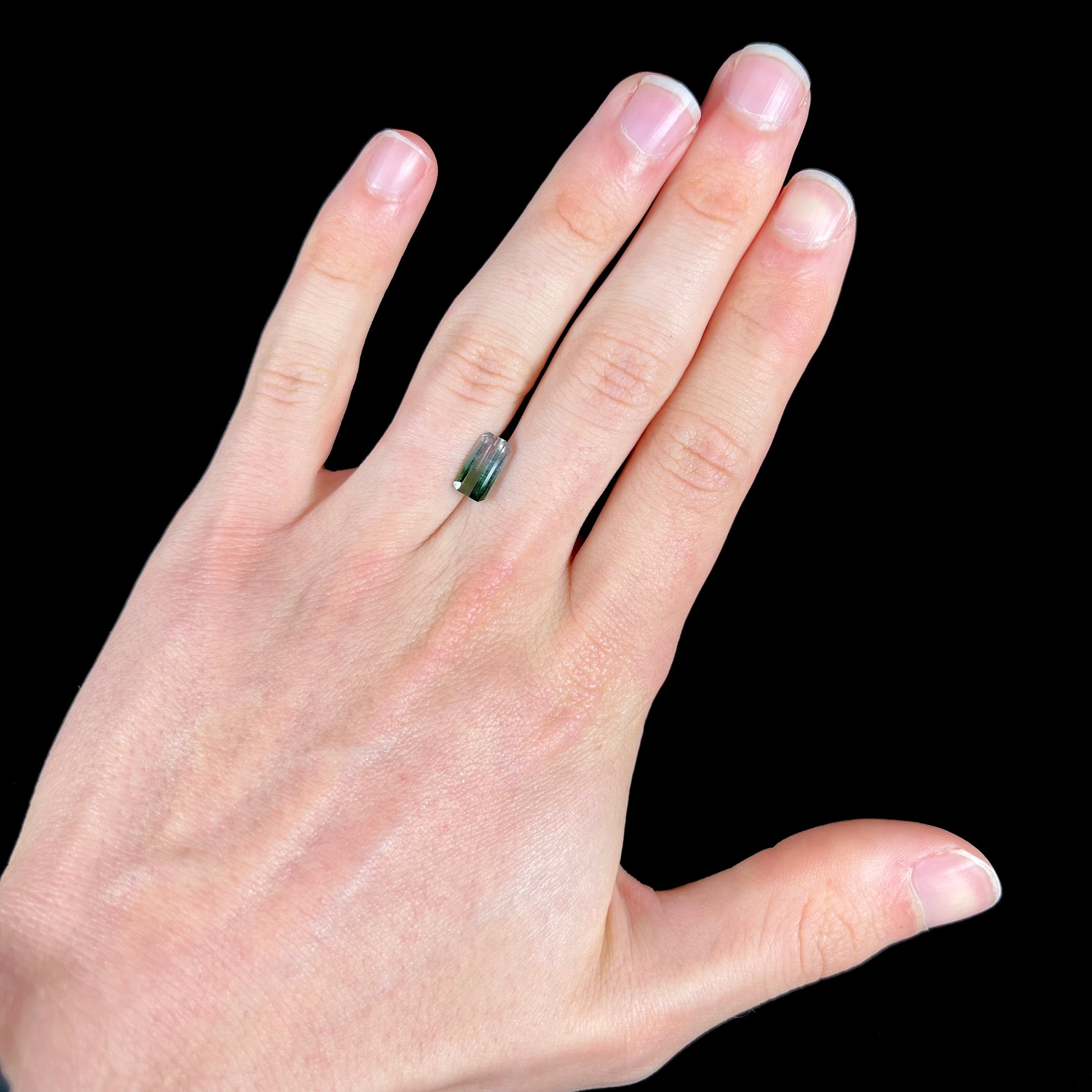 A loose, emerald cut tricolor tourmaline gemstone.  The stone transitions from green to blue to white colors.