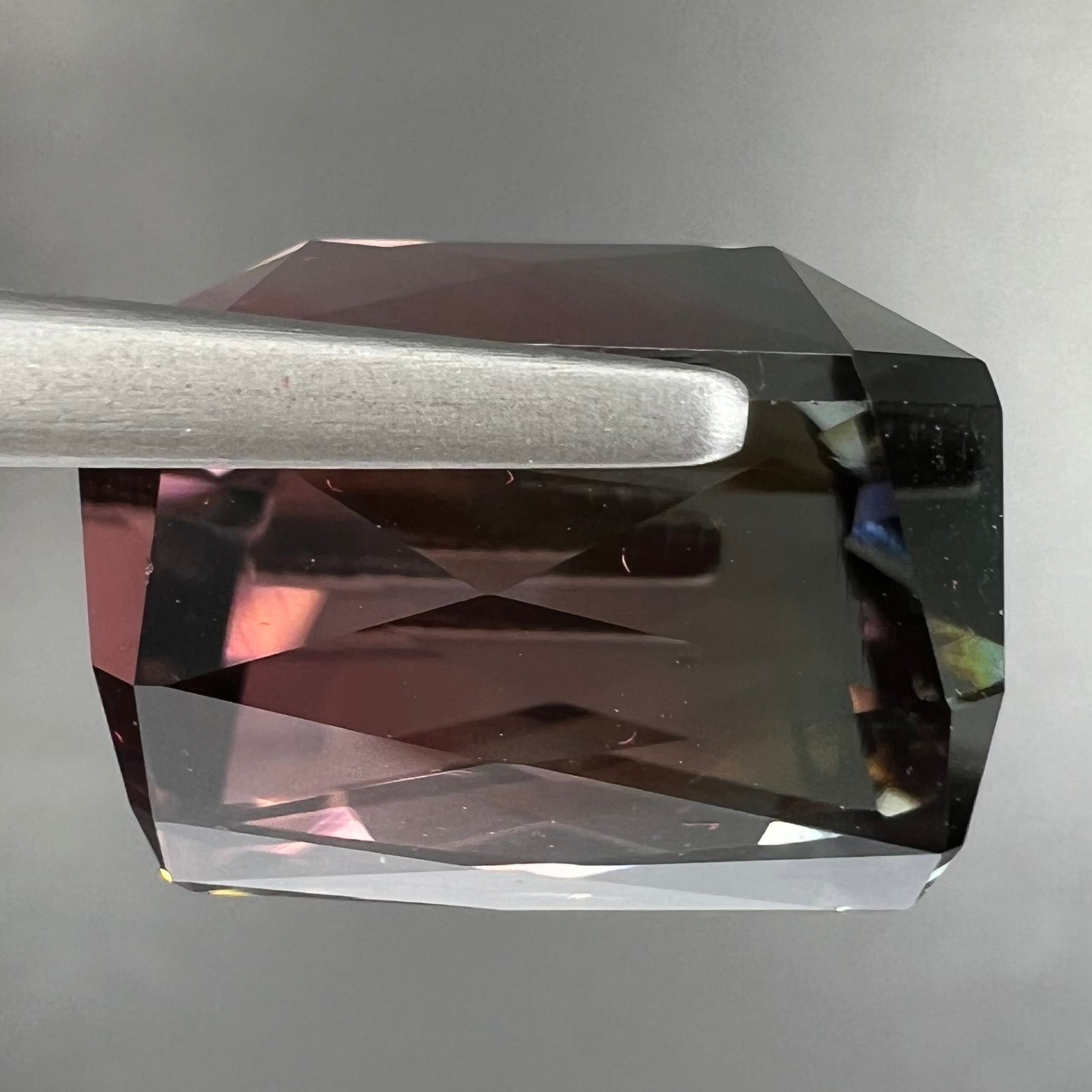A loose, faceted modified emerald cut bicolor tourmaline gemstone.  The stone transitions from dark pink to dark green colors.
