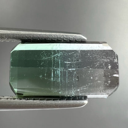 A loose, emerald cut tricolor tourmaline gemstone.  The stone transitions from green to blue to white colors.
