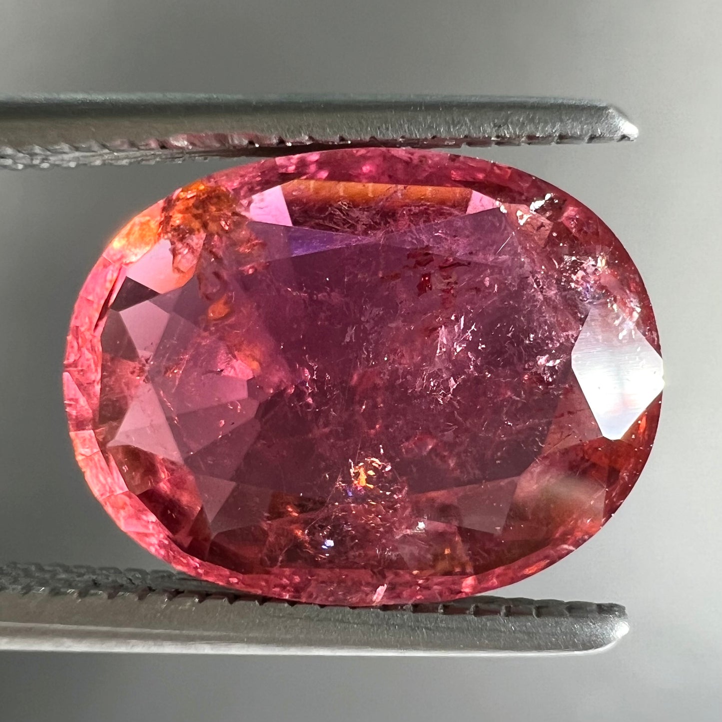 A faceted, oval cut, melon pink tourmaline gemstone.