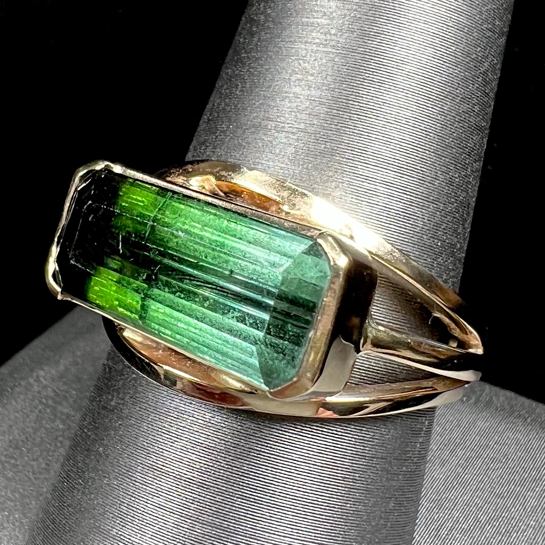 A men's emerald cut tricolor tourmaline solitaire ring in yellow gold.  The tourmaline shifts from green to blue green to blue.