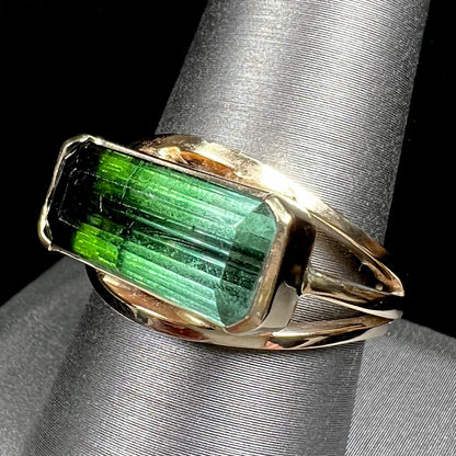 A men's emerald cut tricolor tourmaline solitaire ring in yellow gold.  The tourmaline shifts from green to blue green to blue.