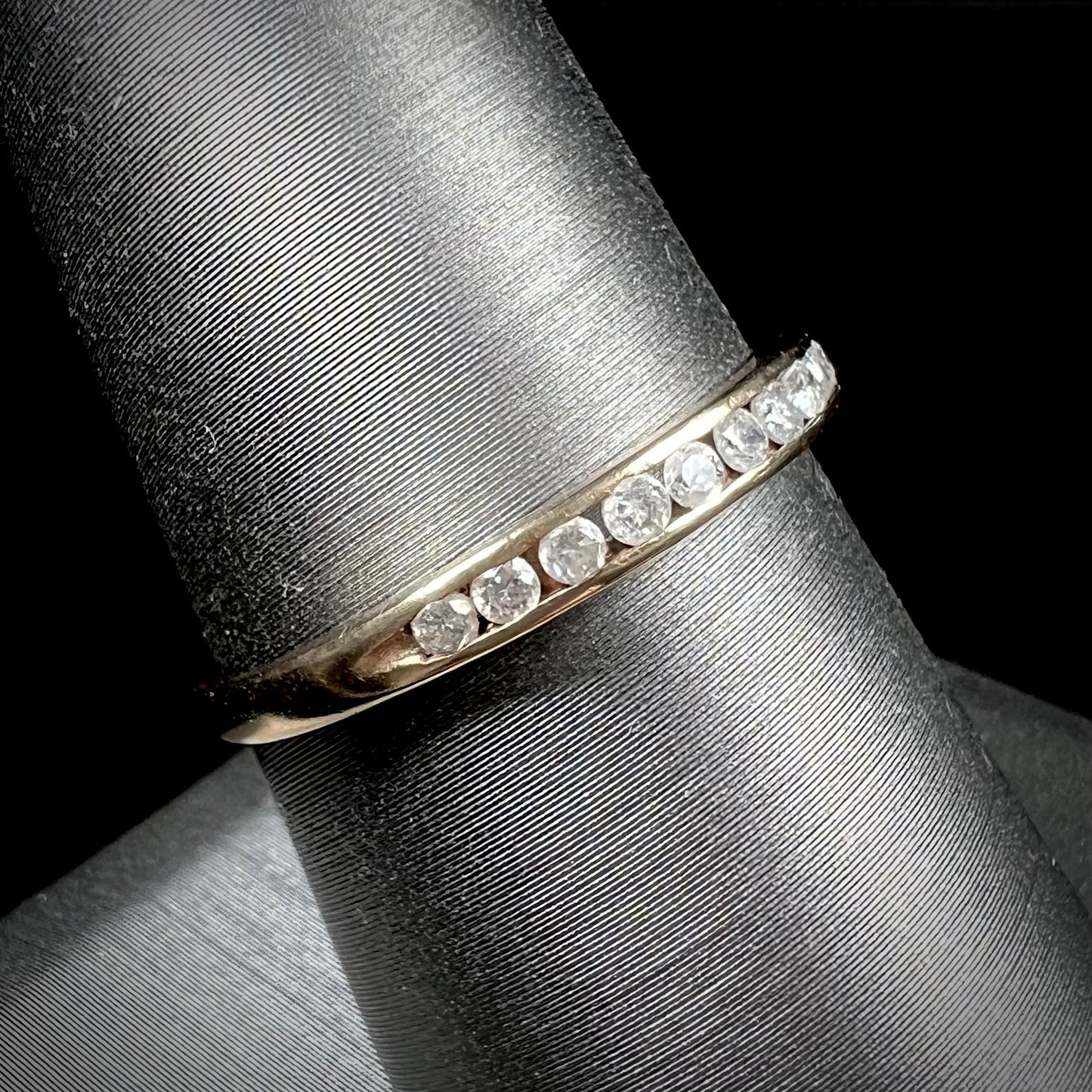 A unisex, thin yellow gold wedding band channel set with 12 round cut diamonds.