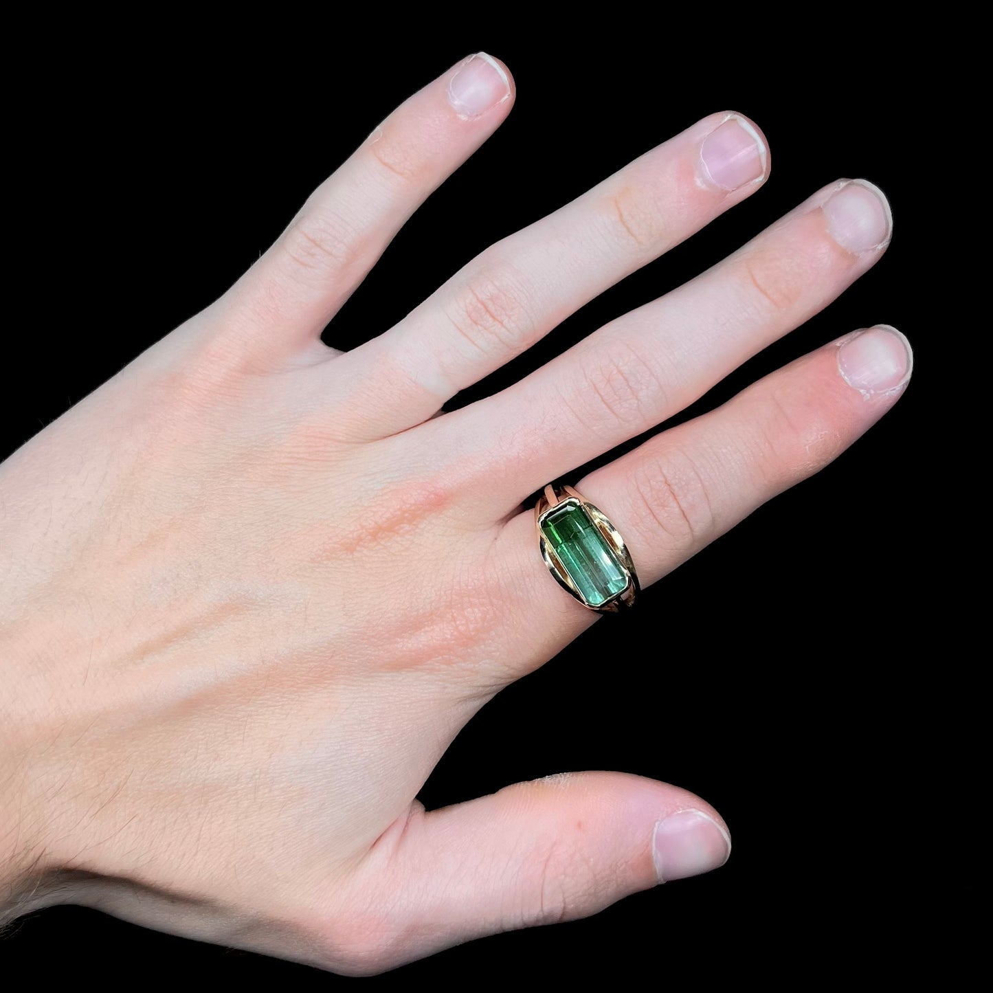 A men's emerald cut tricolor tourmaline solitaire ring in yellow gold.  The tourmaline shifts from green to blue green to blue.