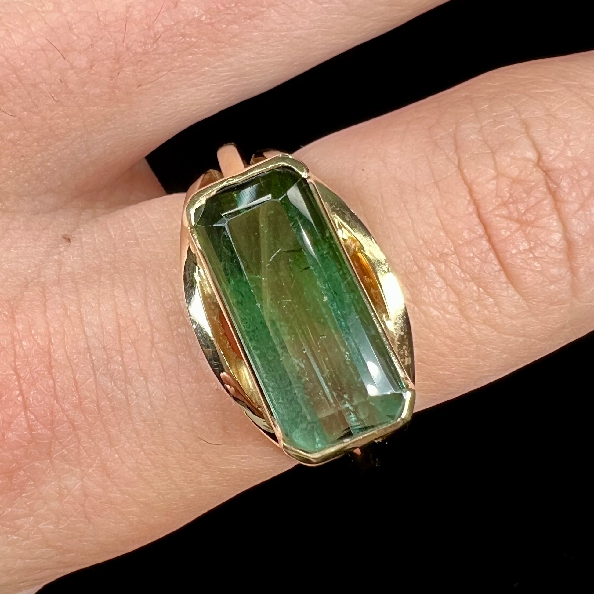 A men's emerald cut tricolor tourmaline solitaire ring in yellow gold.  The tourmaline shifts from green to blue green to blue.