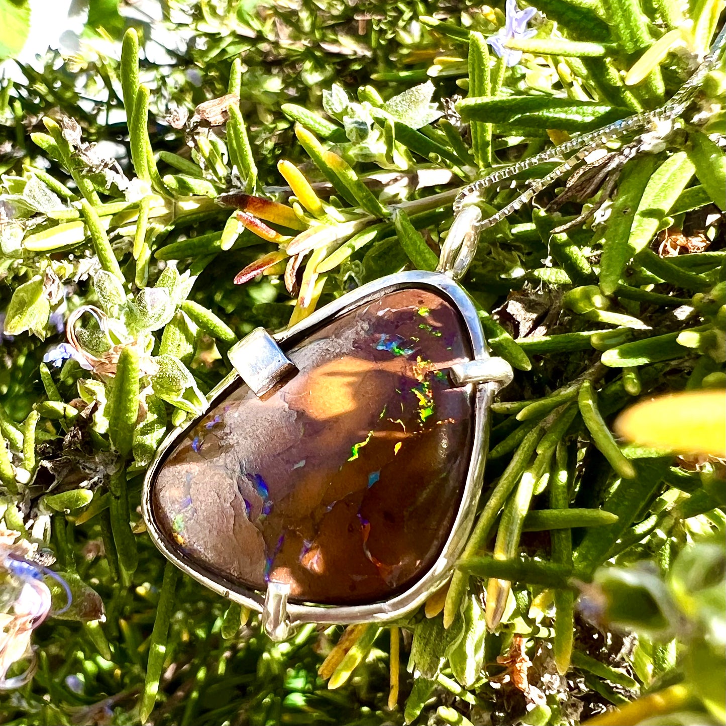 A handmade sterling silver pendant bezel and prong set with a natural boulder opal stone.  The opal shines veins of color.