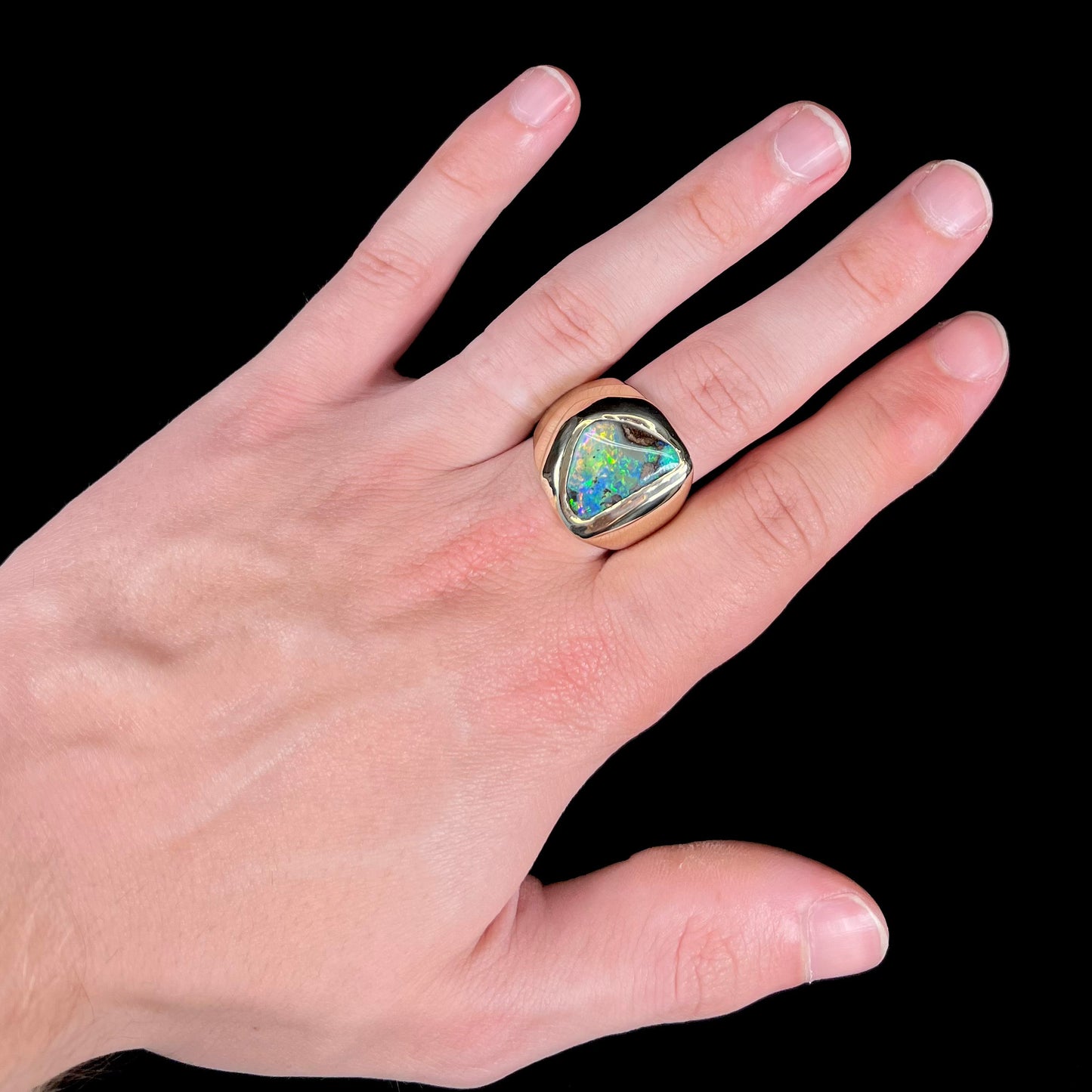 A men's yellow gold solitaire ring set with a triangular shaped natural boulder opal.