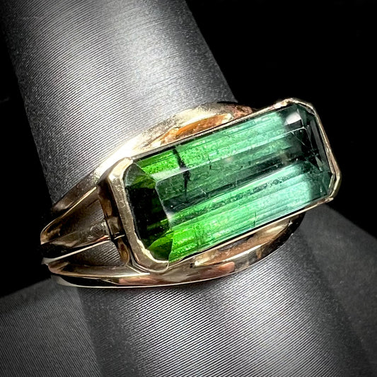 A men's emerald cut tricolor tourmaline solitaire ring in yellow gold.  The tourmaline shifts from green to blue green to blue.