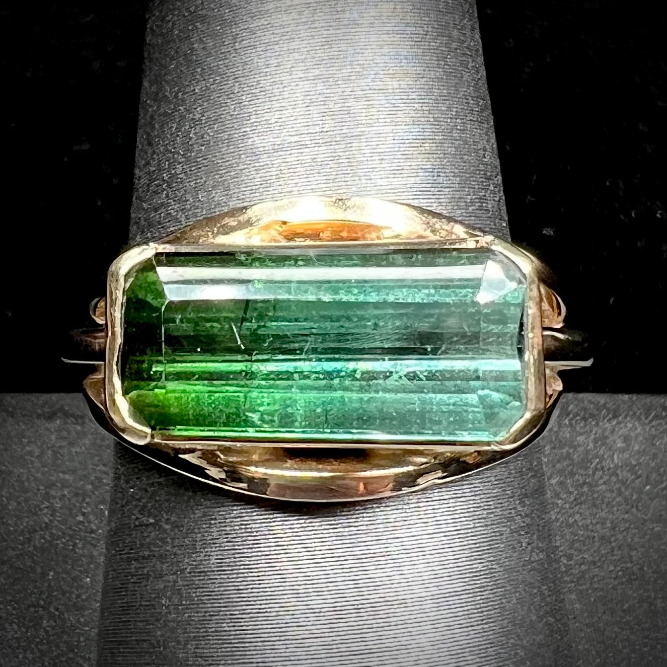 A men's emerald cut tricolor tourmaline solitaire ring in yellow gold.  The tourmaline shifts from green to blue green to blue.