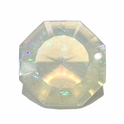 A loose, faceted octagon cut Mexican fire opal gemstone.  The stone is a light yellow color with blue and green fire.