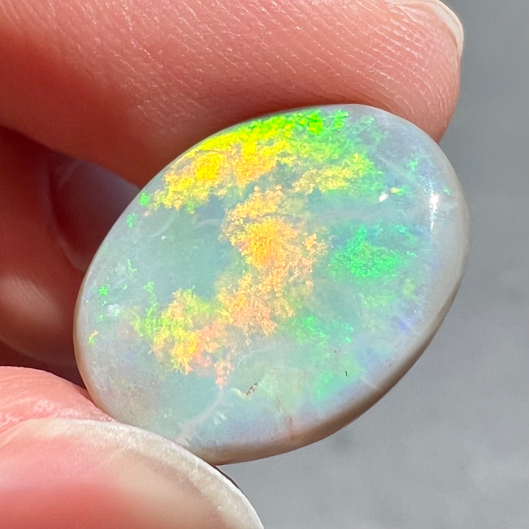 A loose, oval cut light opal stone from Mintabie, Australia.  The stone shows dull orange and green colors.