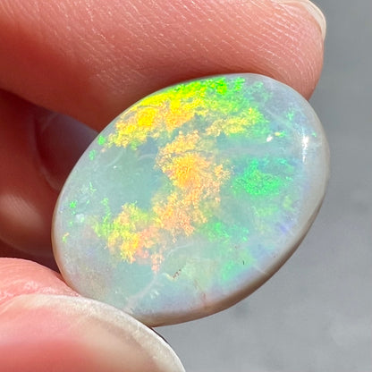 A loose, oval cut light opal stone from Mintabie, Australia.  The stone shows dull orange and green colors.