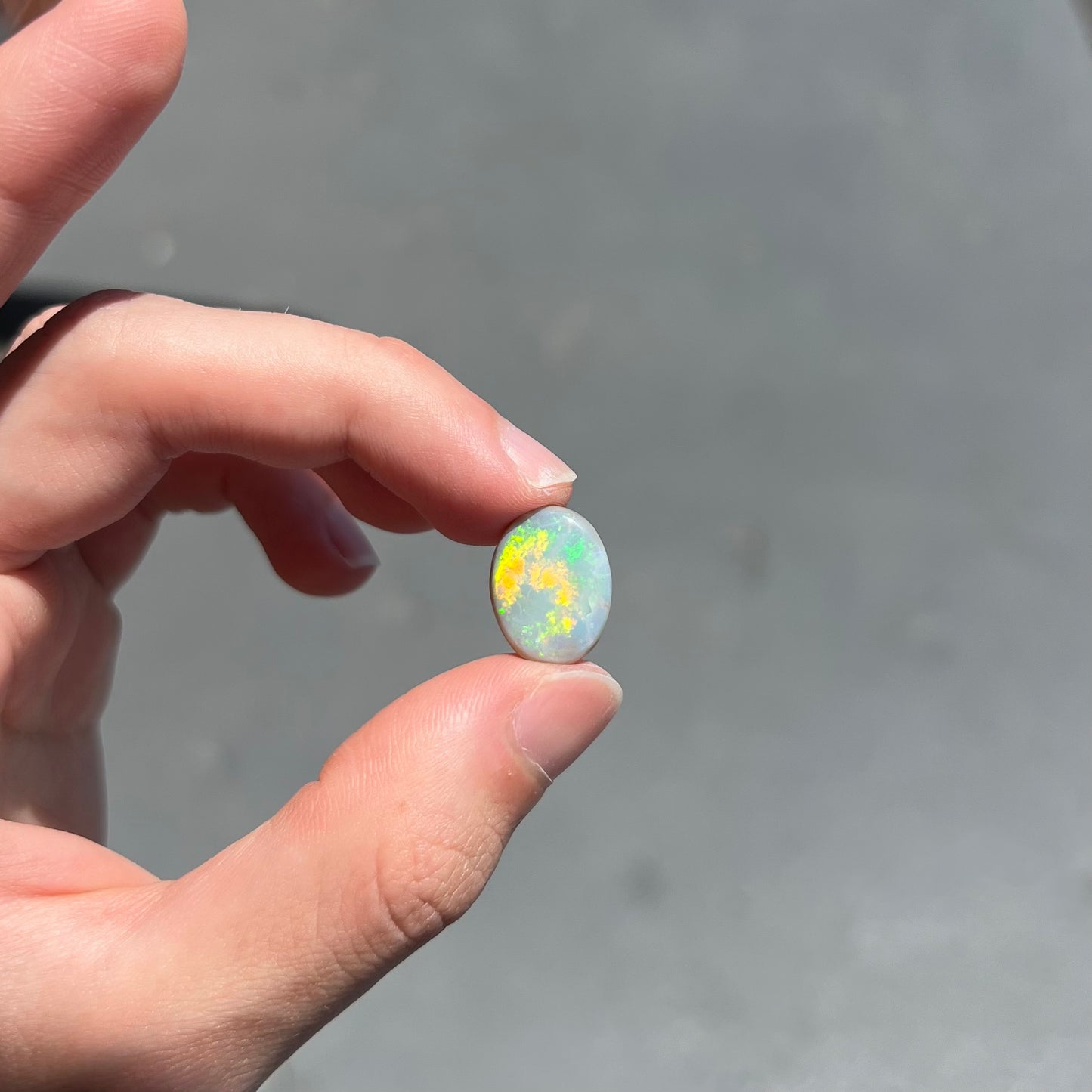 A loose, oval cut light opal stone from Mintabie, Australia.  The stone shows dull orange and green colors.