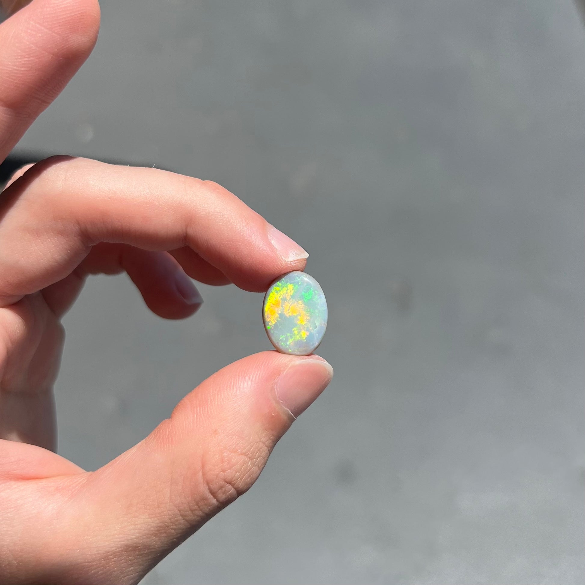 A loose, oval cut light opal stone from Mintabie, Australia.  The stone shows dull orange and green colors.