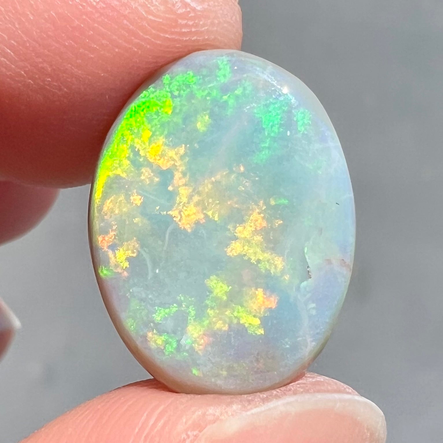 A loose, oval cut light opal stone from Mintabie, Australia.  The stone shows dull orange and green colors.