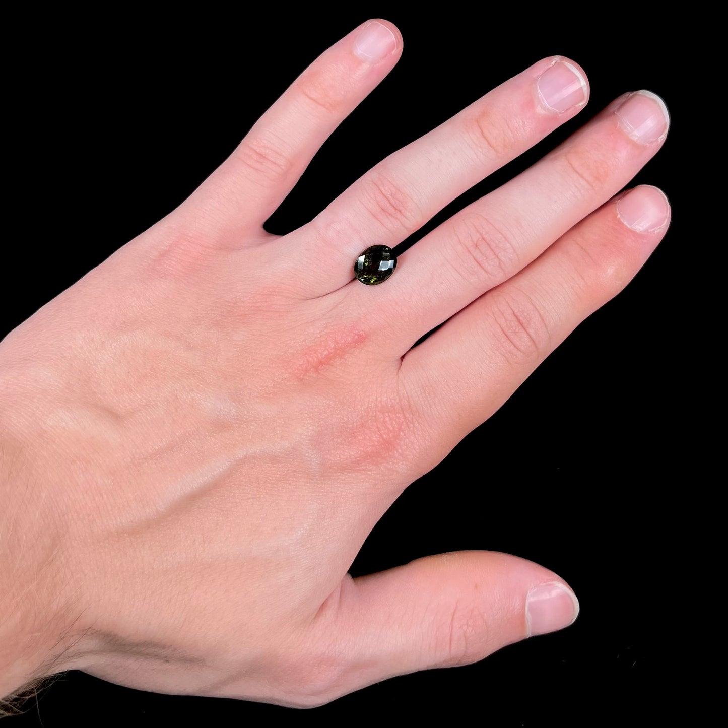 A loose, faceted oval checkerboard moldavite gemstone from the Czech Republic.