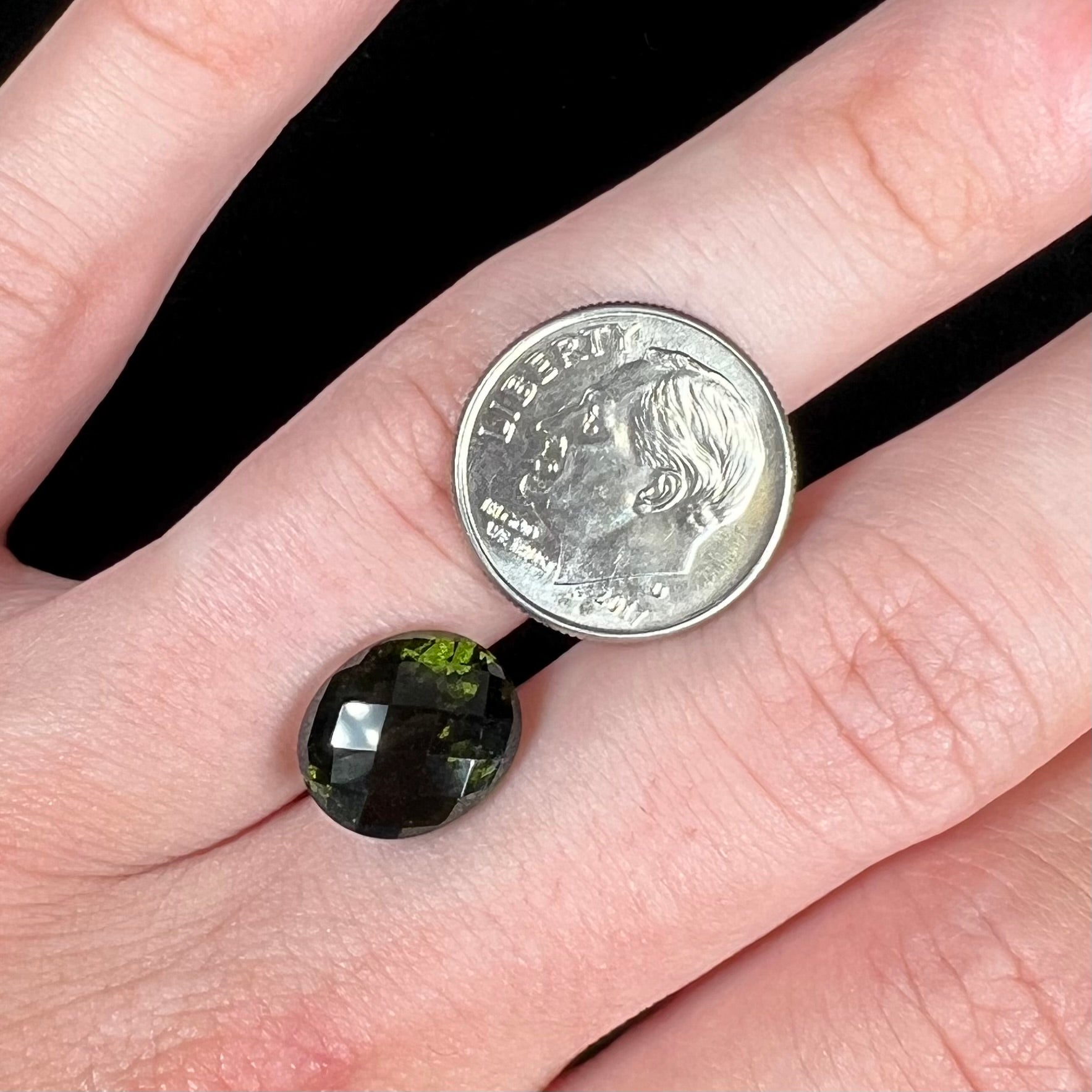 A loose, oval checkerboard cut natural moldavite gemstone.  The stone is dark green color.