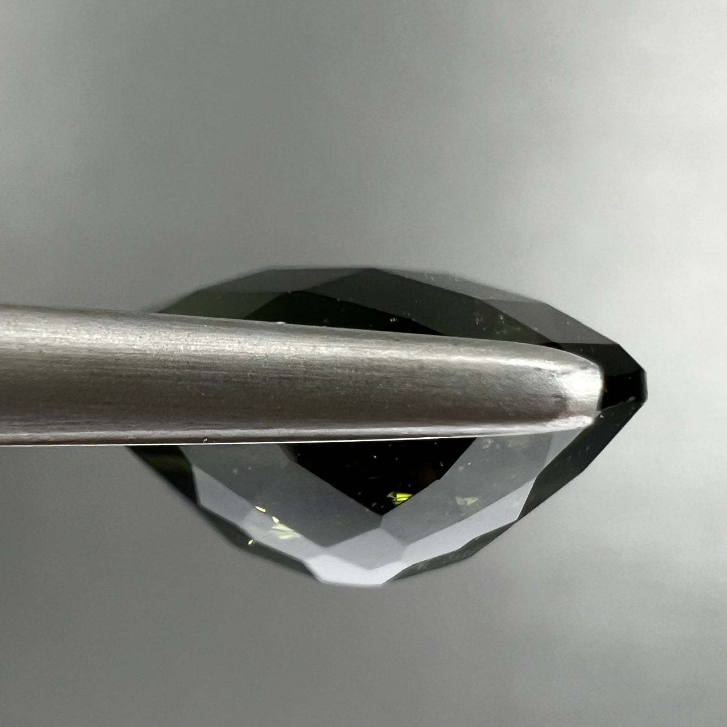 A loose, oval checkerboard cut natural moldavite gemstone.  The stone is dark green color.