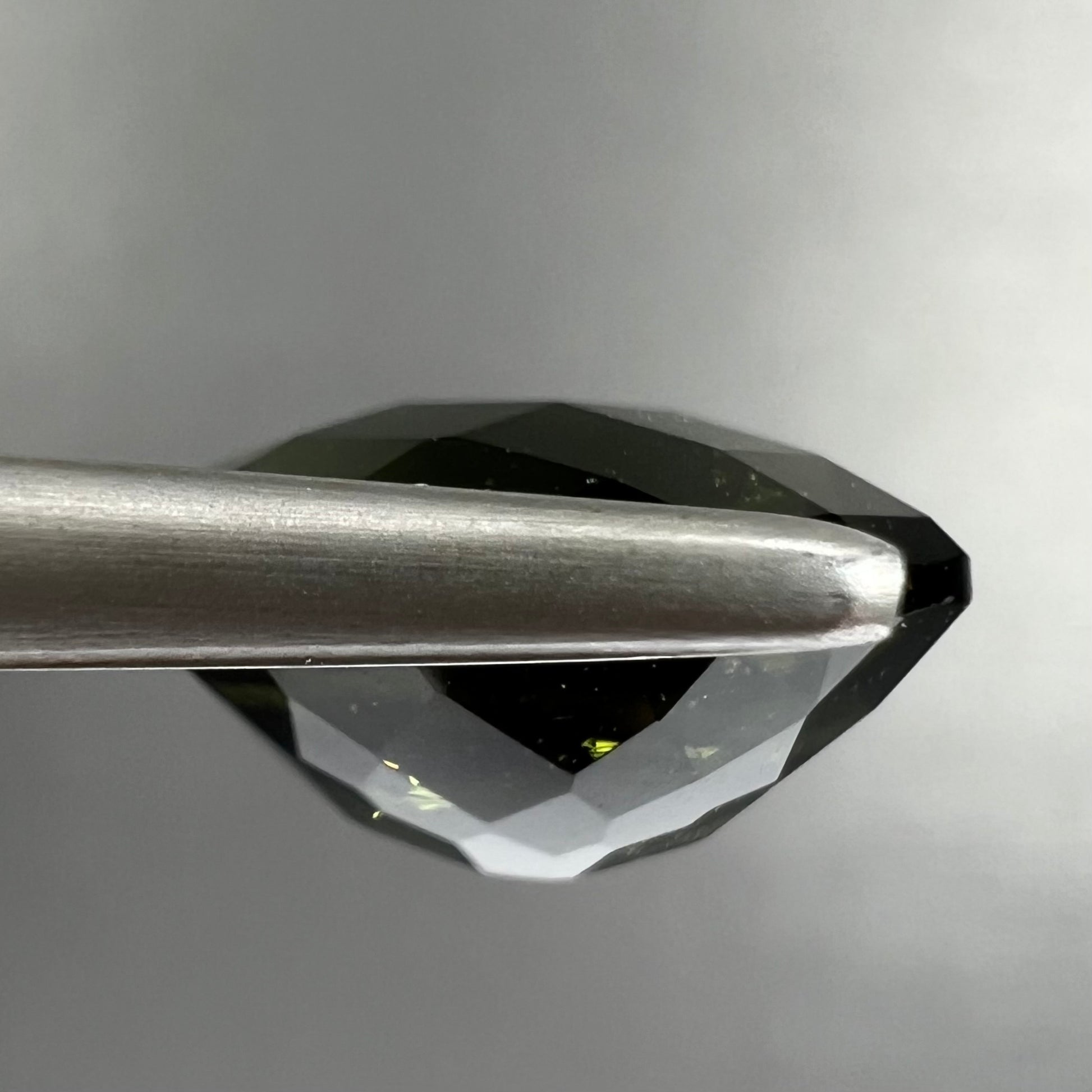 A loose, oval checkerboard cut natural moldavite gemstone.  The stone is dark green color.