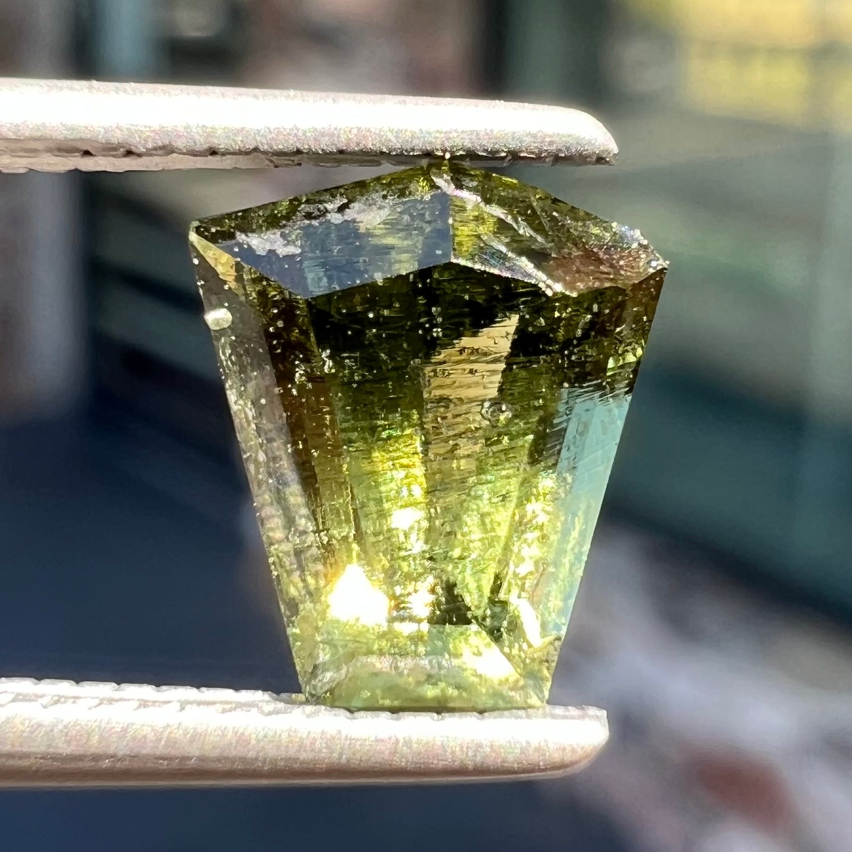 A loose, shield cut, natural moldavite gemstone.  The stone has a small chip in the top corner facet.