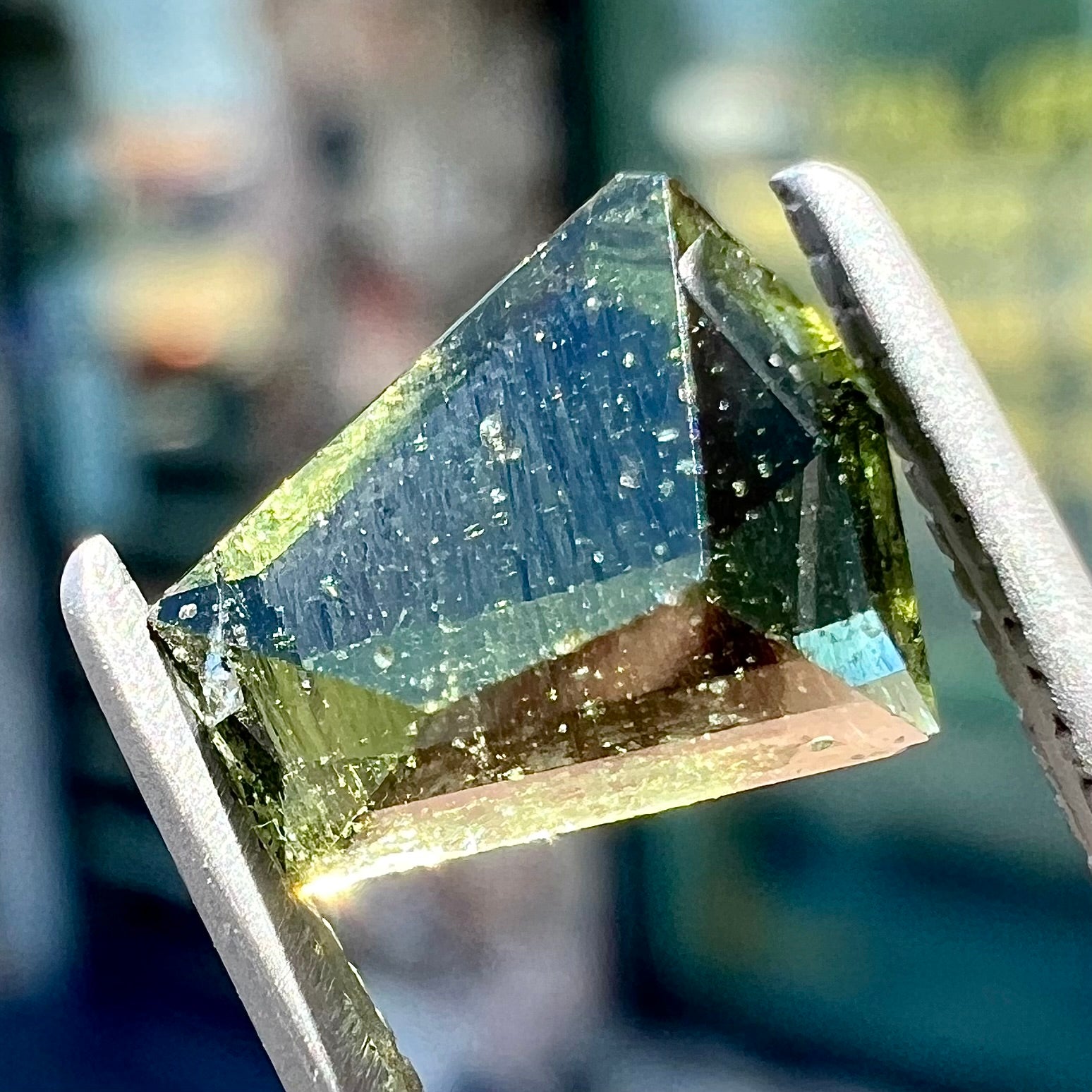 A loose, shield cut, natural moldavite gemstone.  The stone has a small chip in the top corner facet.