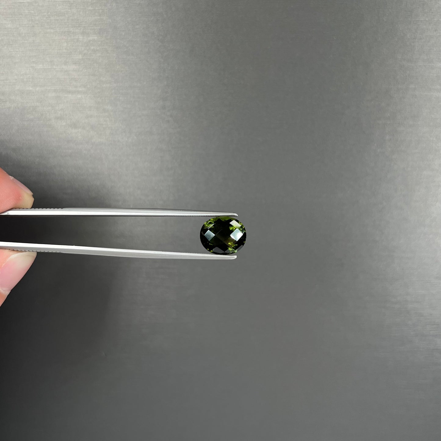 A loose, oval checkerboard cut natural moldavite gemstone.  The stone is dark green color.