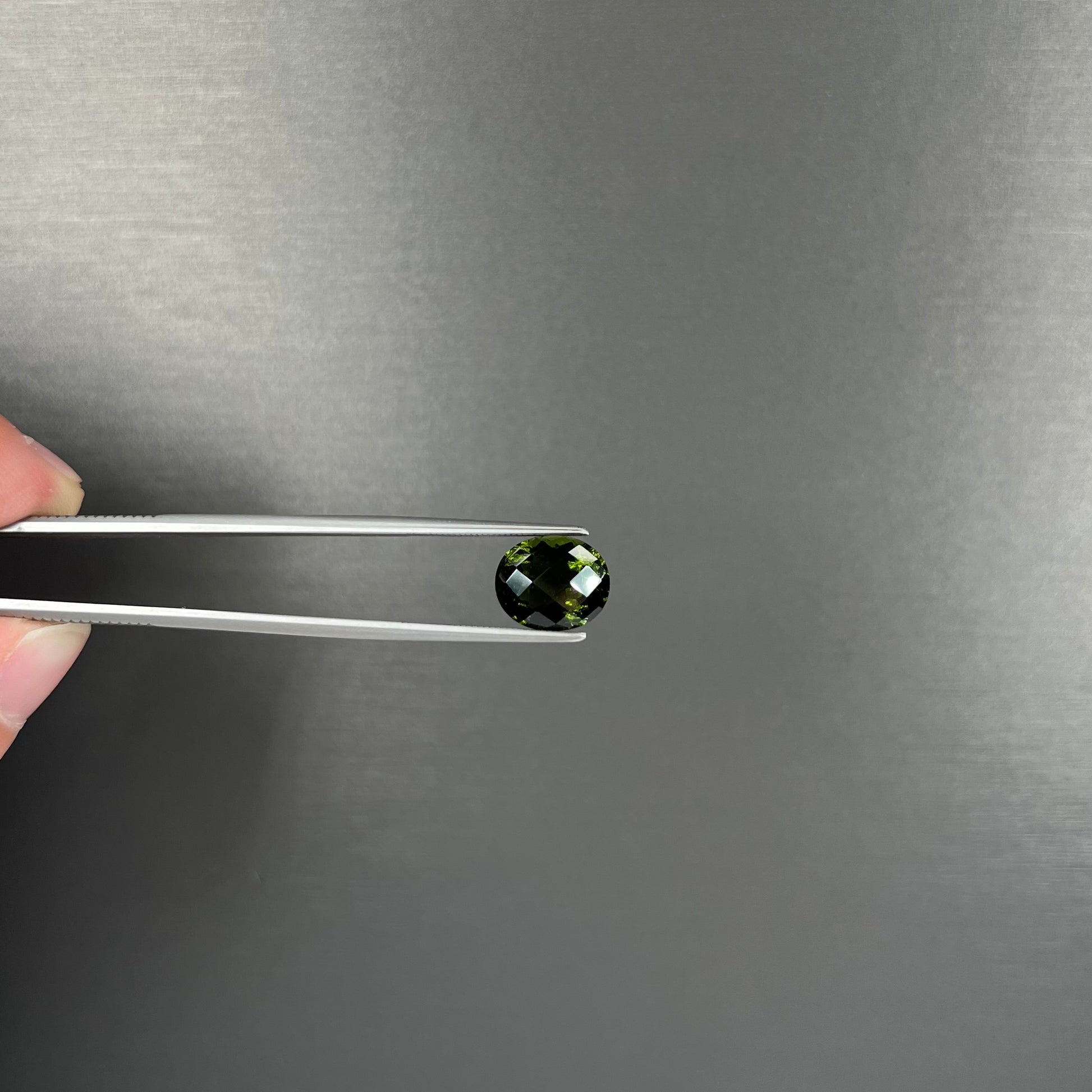 A loose, oval checkerboard cut natural moldavite gemstone.  The stone is dark green color.