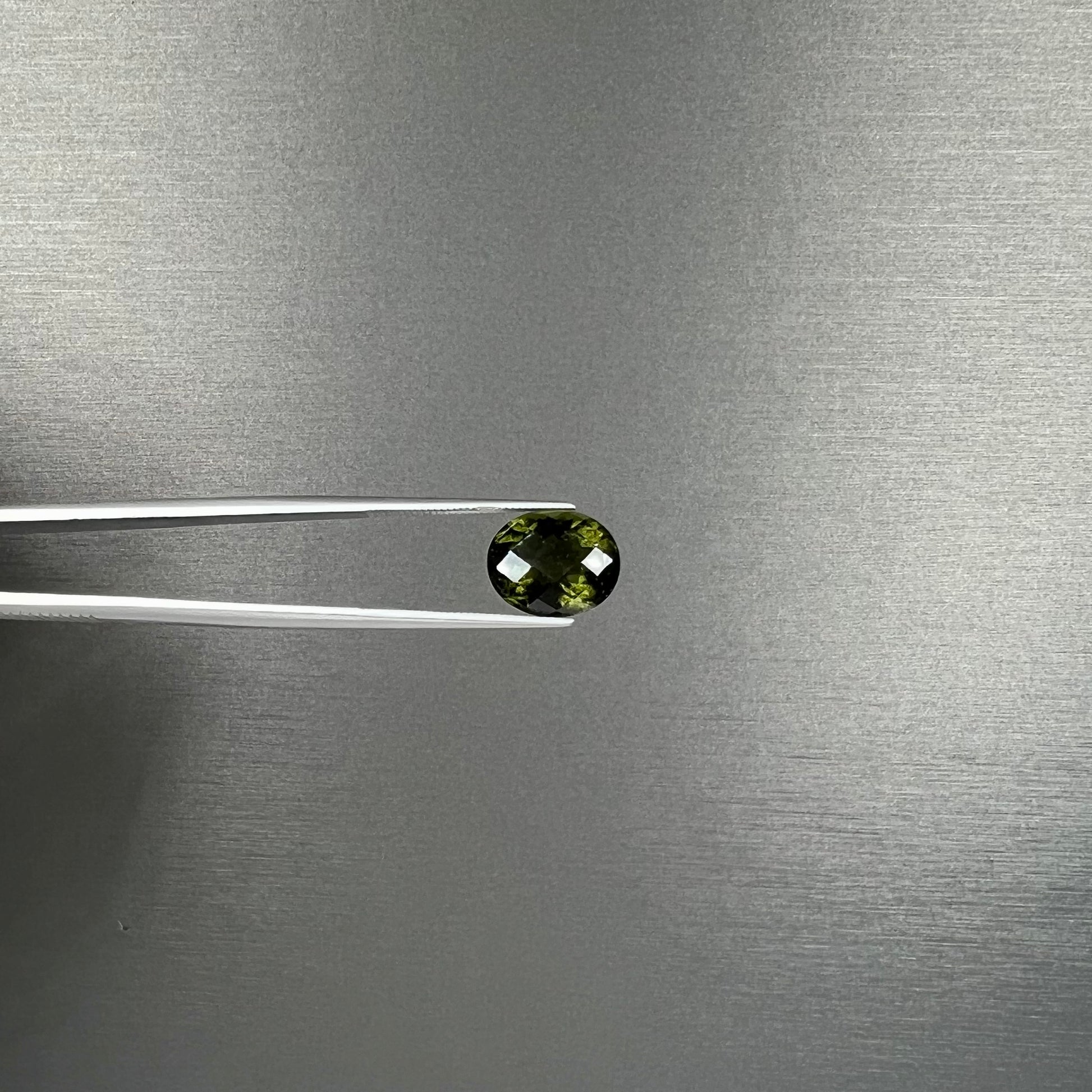 A loose, faceted oval cut natural moldavite gemstone.