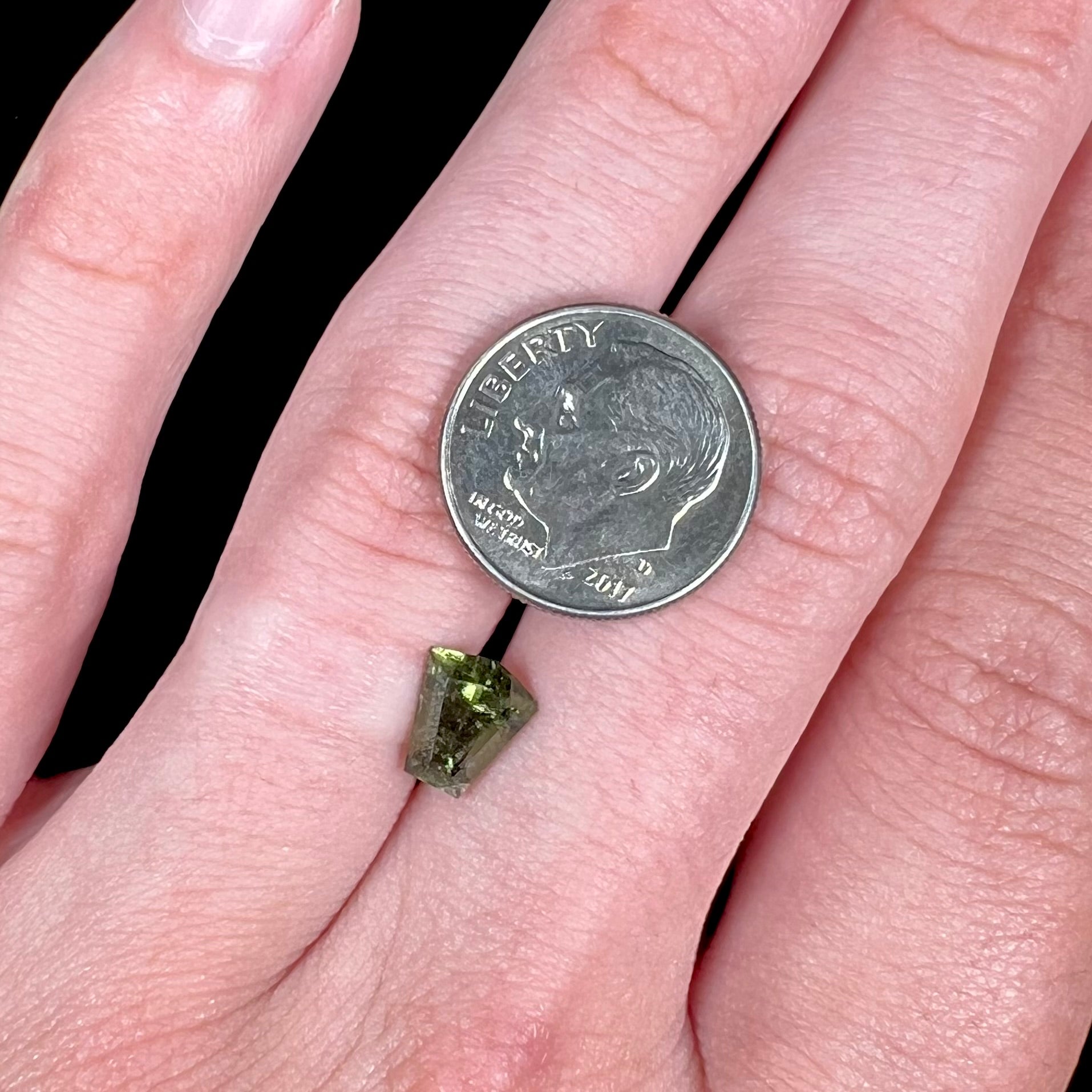 A loose, shield cut, natural moldavite gemstone.  The stone has a small chip in the top corner facet.