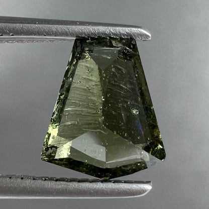 A loose, shield cut, natural moldavite gemstone.  The stone has a small chip in the top corner facet.
