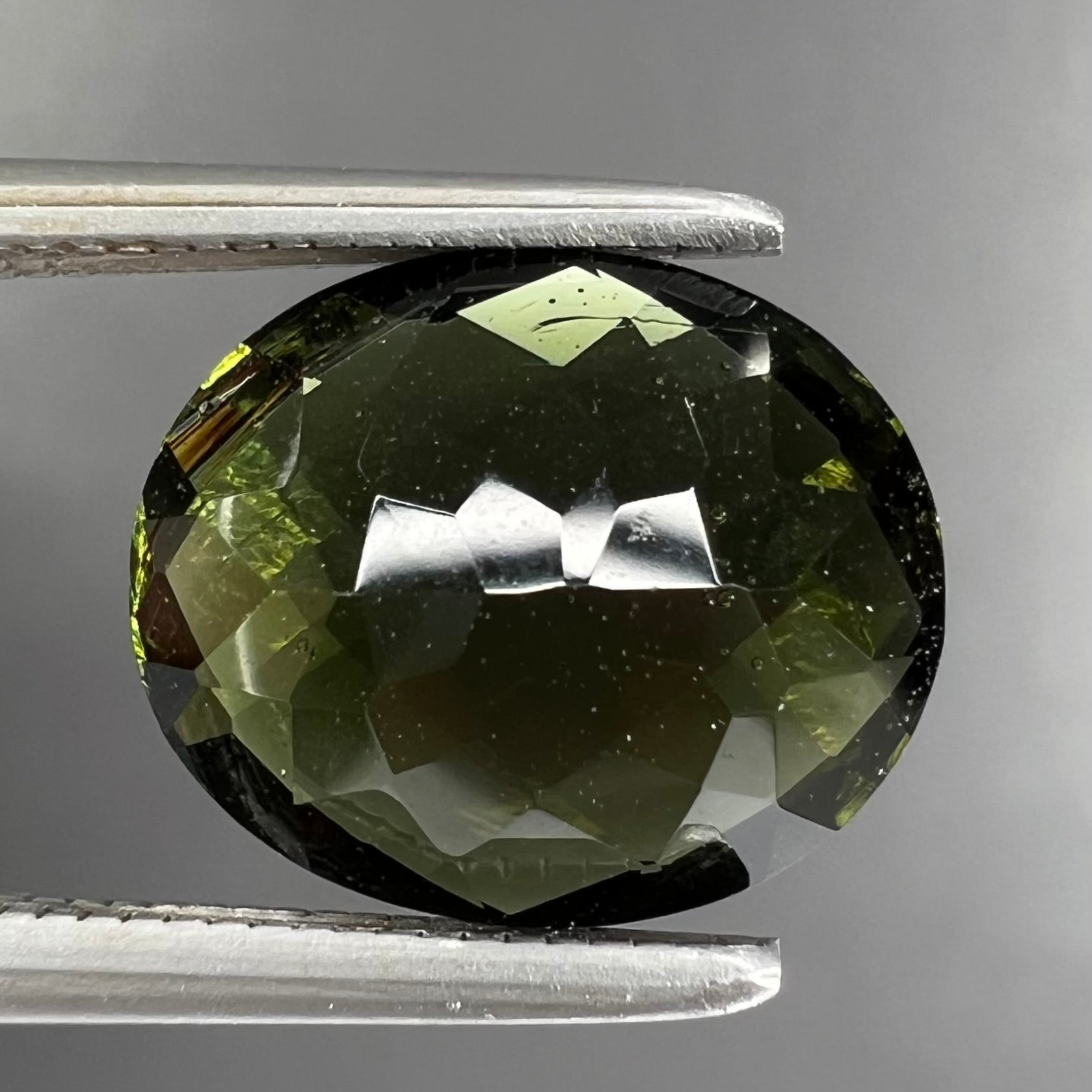 A loose, oval checkerboard cut natural moldavite gemstone.  The stone is dark green color.