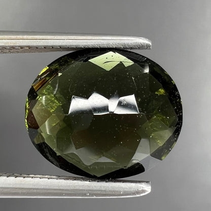 A loose, oval checkerboard cut natural moldavite gemstone.  The stone is dark green color.