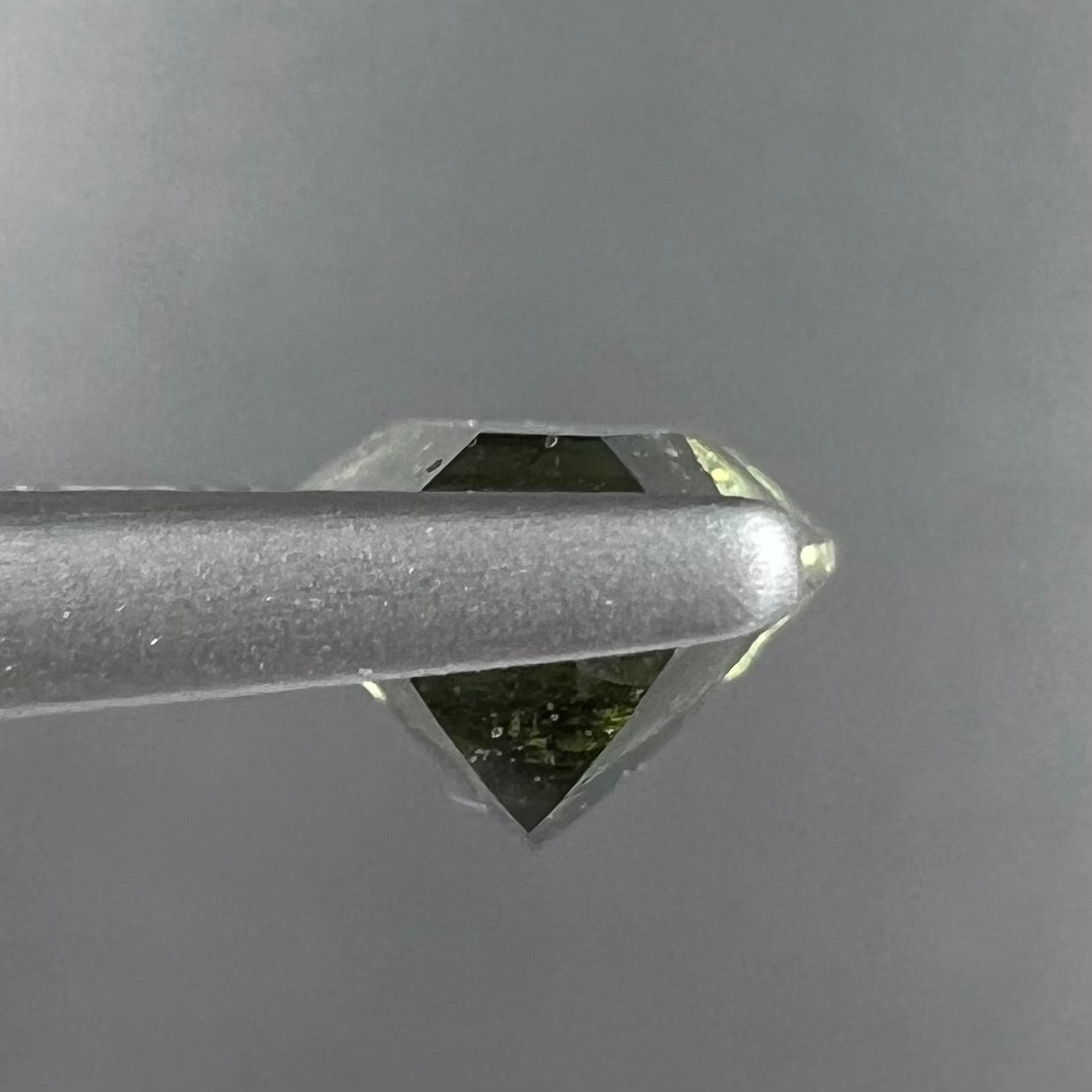 A loose, shield cut, natural moldavite gemstone.  The stone has a small chip in the top corner facet.