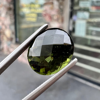 A loose, oval checkerboard cut natural moldavite gemstone.  The stone is dark green color.