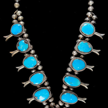 A sterling silver, Navajo style squash blossom necklace set with Morenci turquoise stones.  The legnth is designed for women and children.