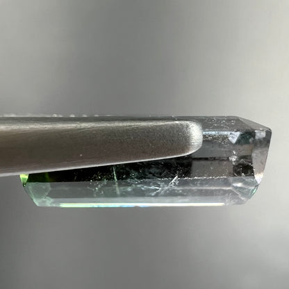 A loose, emerald cut tricolor tourmaline gemstone.  The stone transitions from green to blue to white colors.