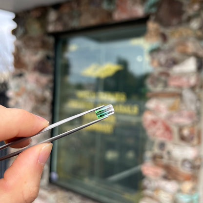 A loose, emerald cut tricolor tourmaline gemstone.  The stone transitions from green to blue to white colors.