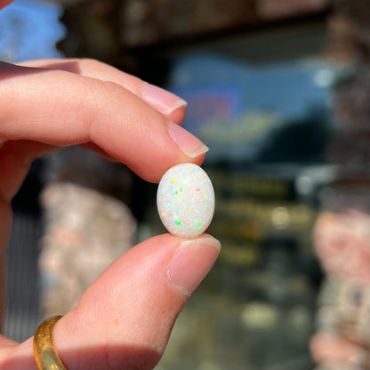 An oval cabochon cut white opal.  The opal has an eye-visible natural fissure inclusion.