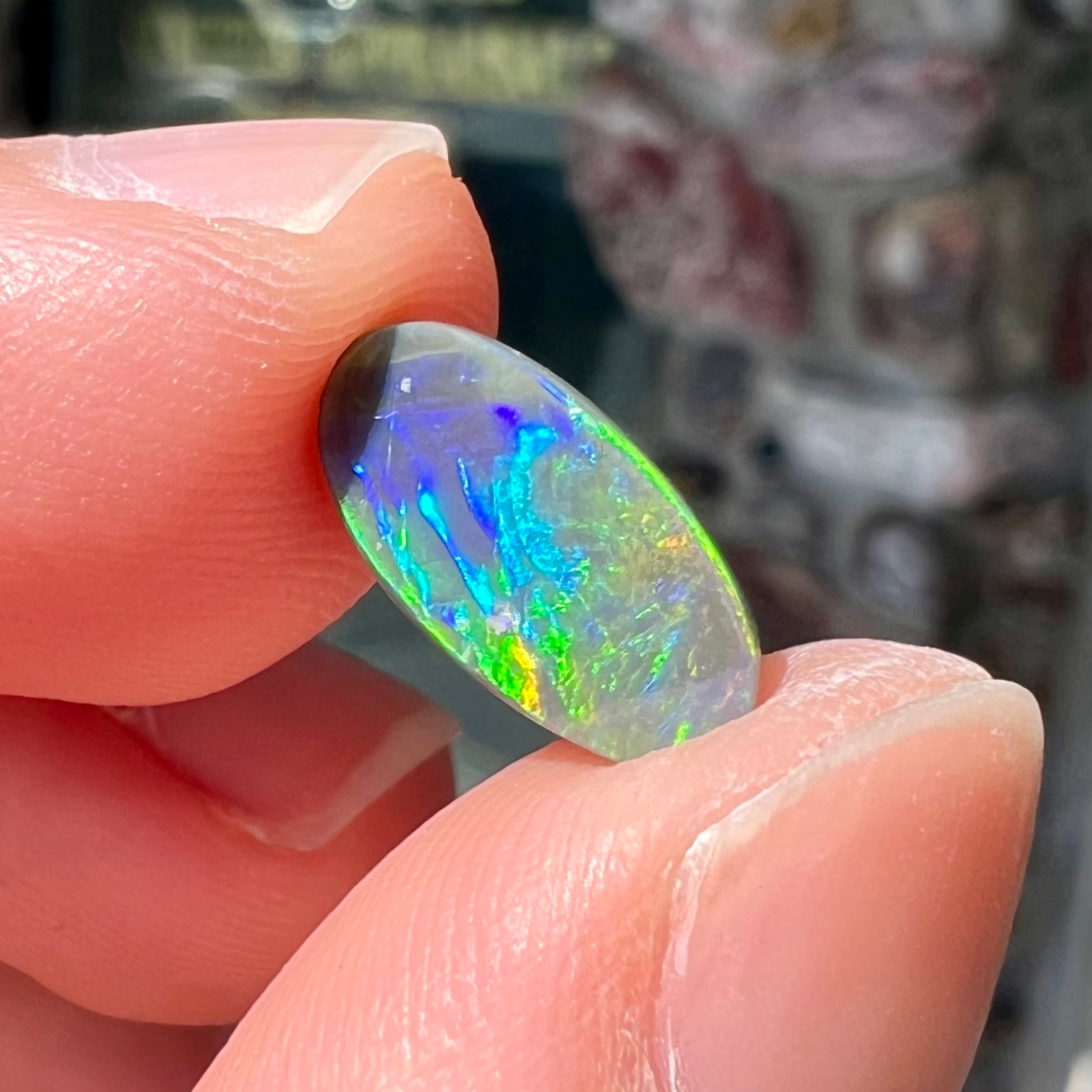 A loose, oval shaped black opal stone from Lightning Ridge, Australia.  The opal plays bright green and blue colors.
