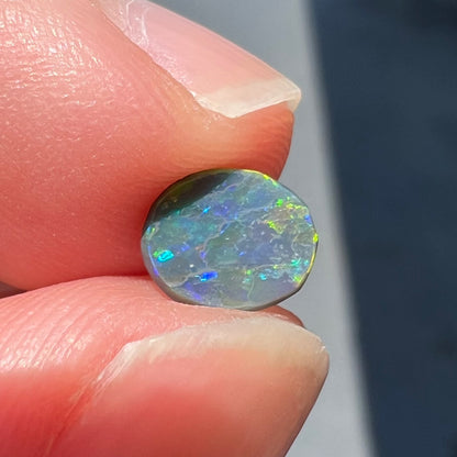 A loose oval cabochon cut black opal from Lightning Ridge, Australia.  The opal shows green and red colors.