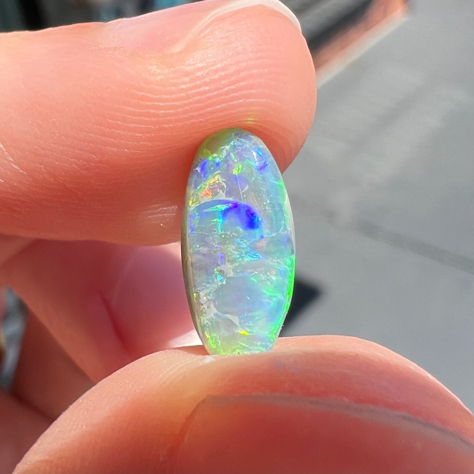 A loose, oval cabochon cut semi-black opal from Lightning Ridge, Australia.  The opal plays green and orange colors.