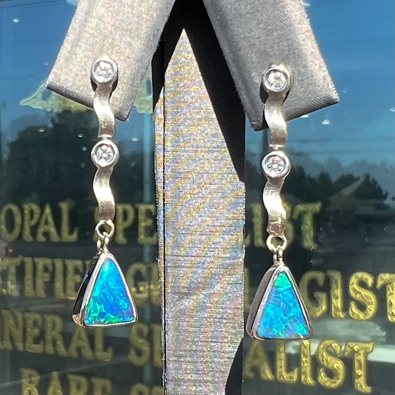 A pair of white gold earrings set with triangle cut natural black opals and round diamond accents.
