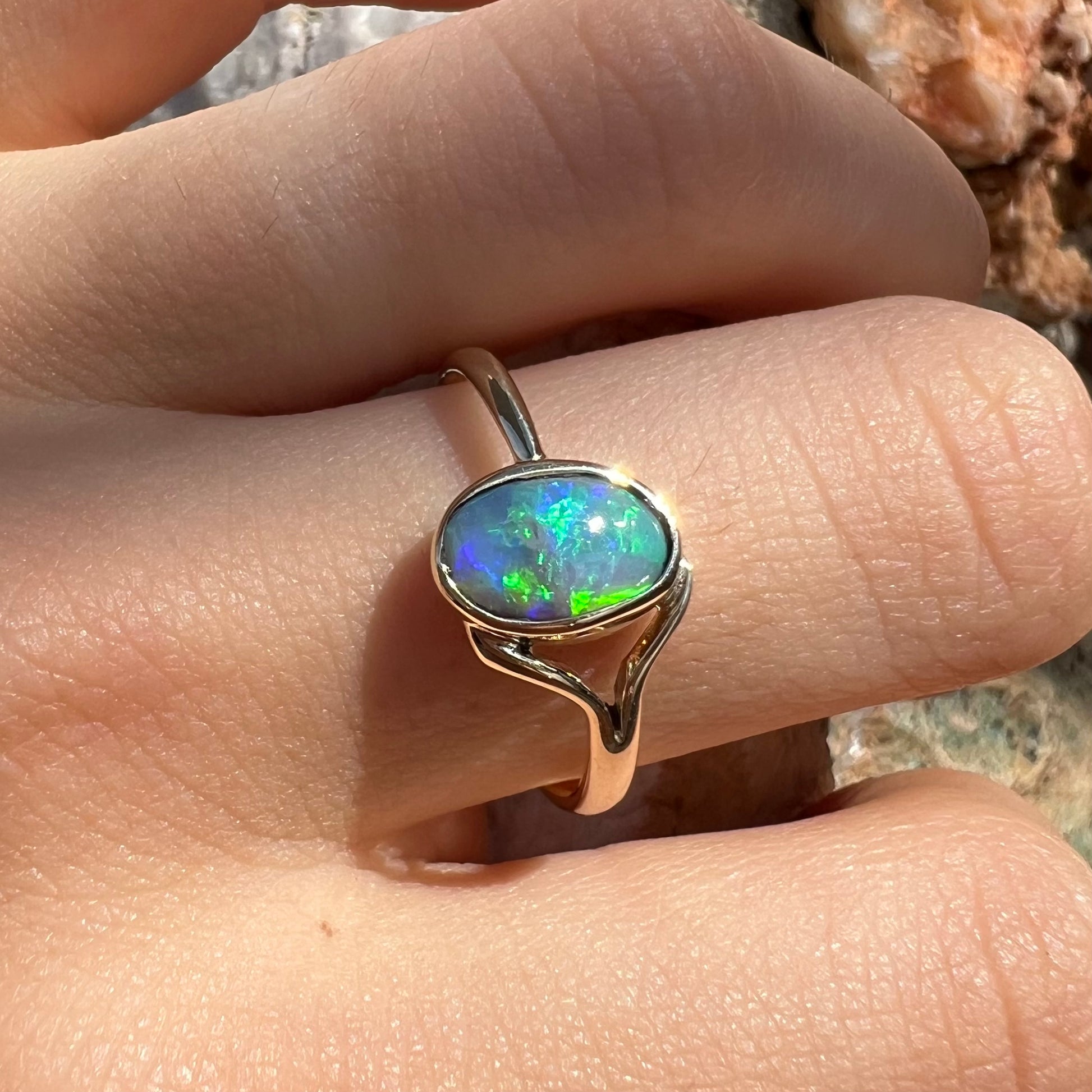 A ladies' oval cut black crystal opal solitaire ring handmade with a single split shank in yellow gold.