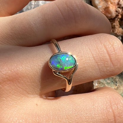 A ladies' oval cut black crystal opal solitaire ring handmade with a single split shank in yellow gold.